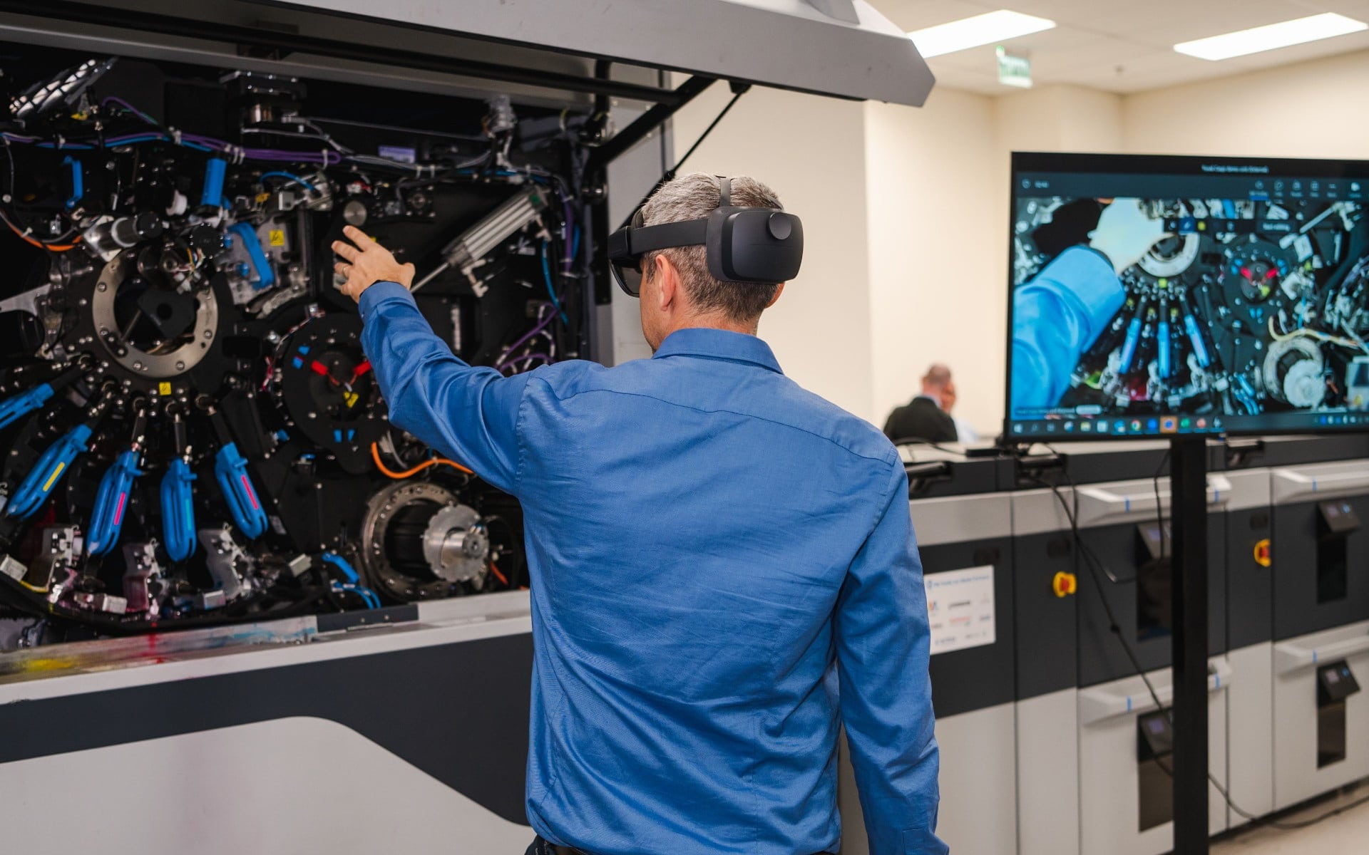 Man wearing HoloLens VR glasses, reaching out to HP Indigo digital press 